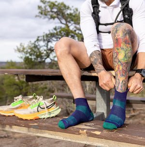 Person sitting on a wooden bench wearing colorful socks and shoes, with a tattooed leg.