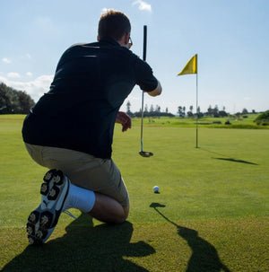 Golfer preparing to putt on a green with a yellow flag in the background